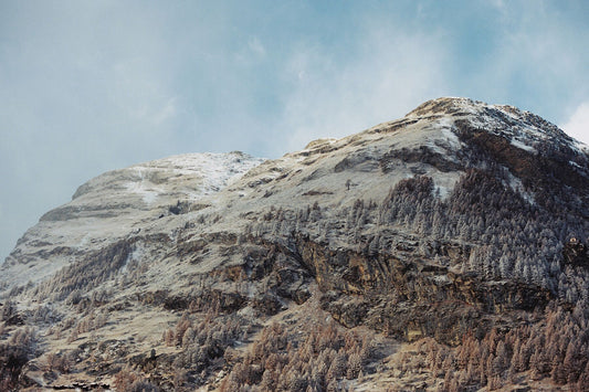 Analog mountain landscape print of alpine peaks between seasons with light snow and exposed rock, shot on 35mm film in the Swiss Alps under soft blue sky