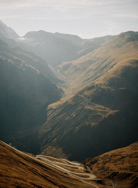 Analog mountain valley landscape print with winding alpine road between golden hills, shot on 35mm film in the Swiss Alps under soft natural light