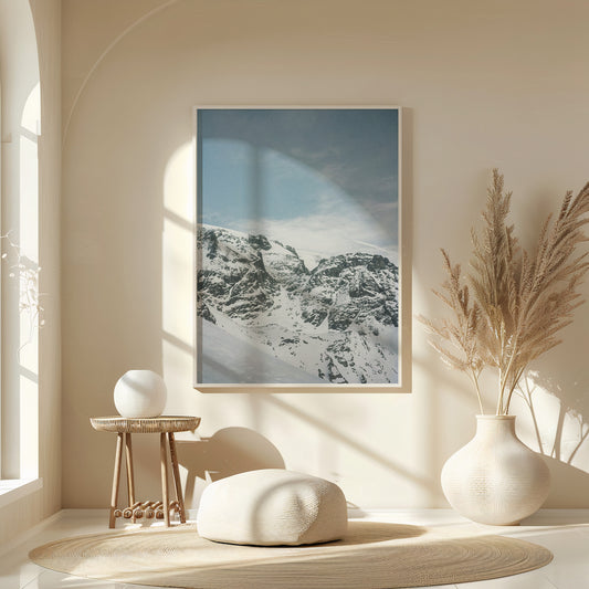 Minimalist interior with a framed snow-covered mountain landscape print in soft blue tones, styled above a wooden console with ceramic vases and natural light, fine art analog photography print shot on 35mm film