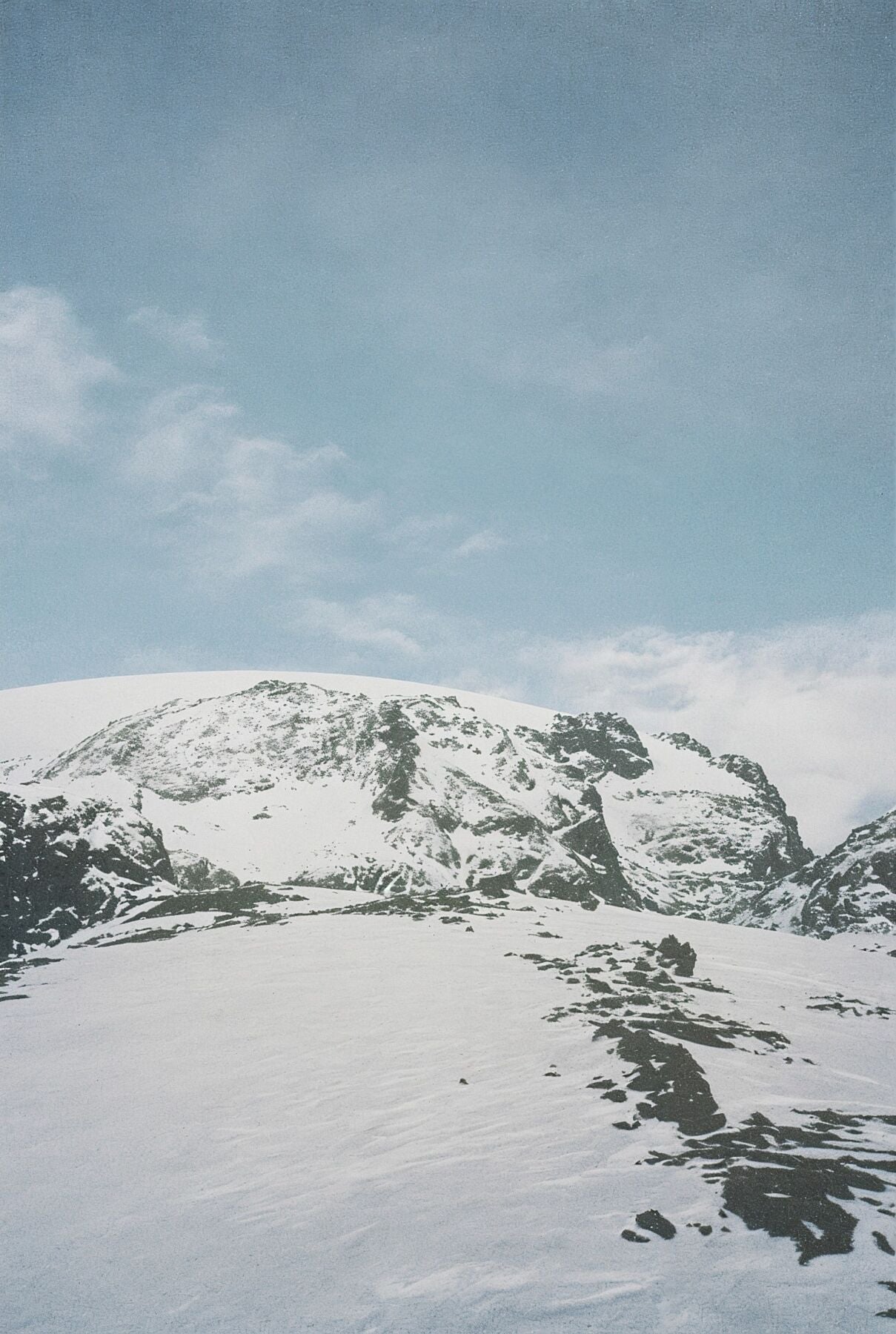 Analog snow covered mountain landscape print with alpine peaks under blue sky, shot on 35mm film in the Swiss Alps with soft natural light
