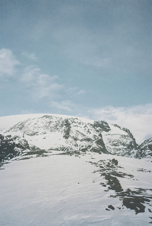 Analog snow covered mountain landscape print with alpine peaks under blue sky, shot on 35mm film in the Swiss Alps with soft natural light
