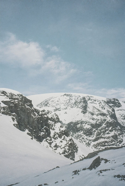 Analog snow covered mountain landscape print with alpine peaks under blue sky, shot on 35mm film in the Swiss Alps with soft natural light