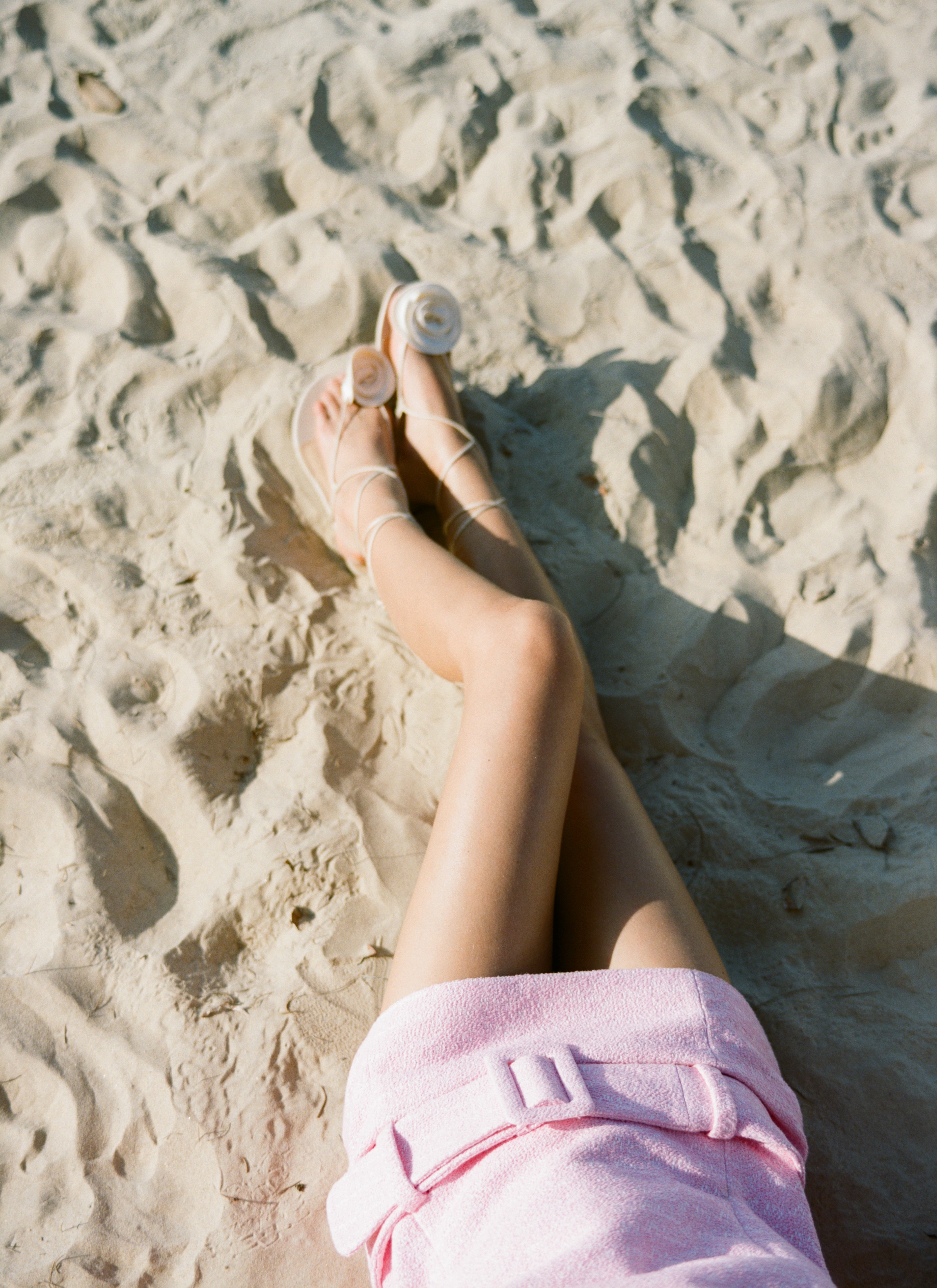 Analog fashion detail of legs wearing a pink Chanel dress on sandy beach, shot on medium format film in soft natural light