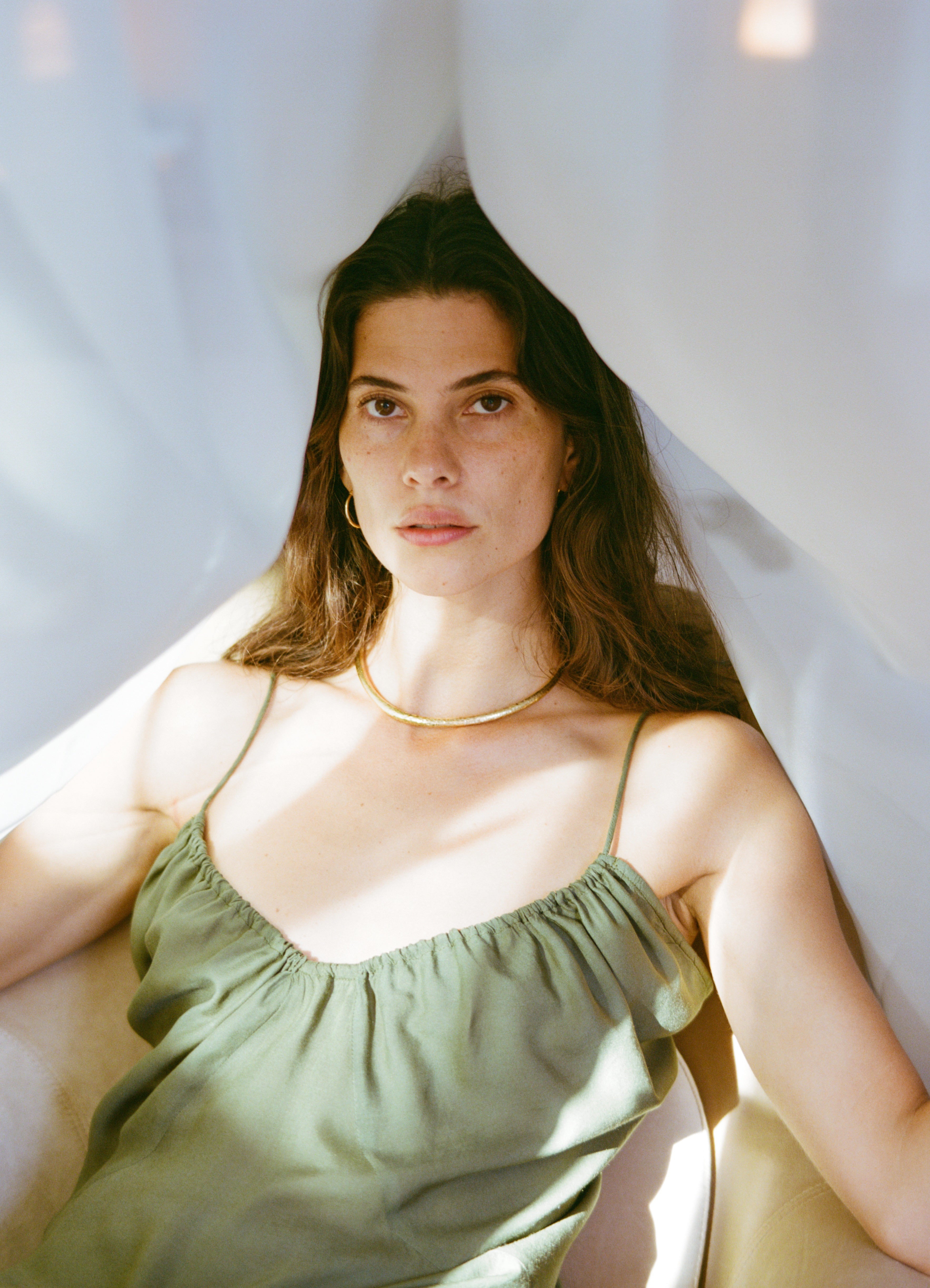 Analog fashion portrait of Courtney wearing Fara Boutique, seated in soft natural light with sheer fabric framing her, shot on medium format film shot in Grace La Magda St Moritz