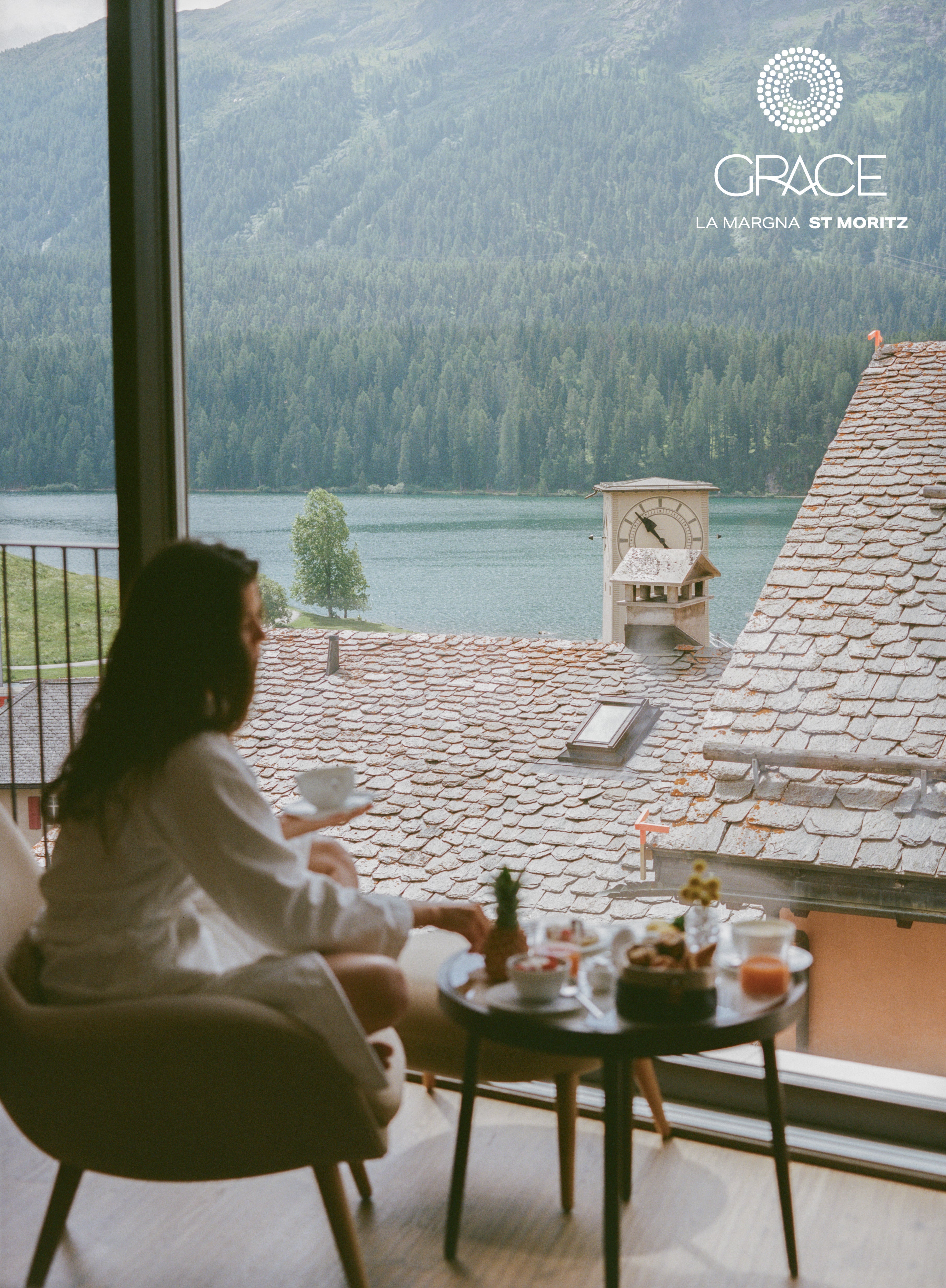Person sitting at a table with a scenic view of mountains and a lake, with 'Grace' branding shot on 120mm St Moritz