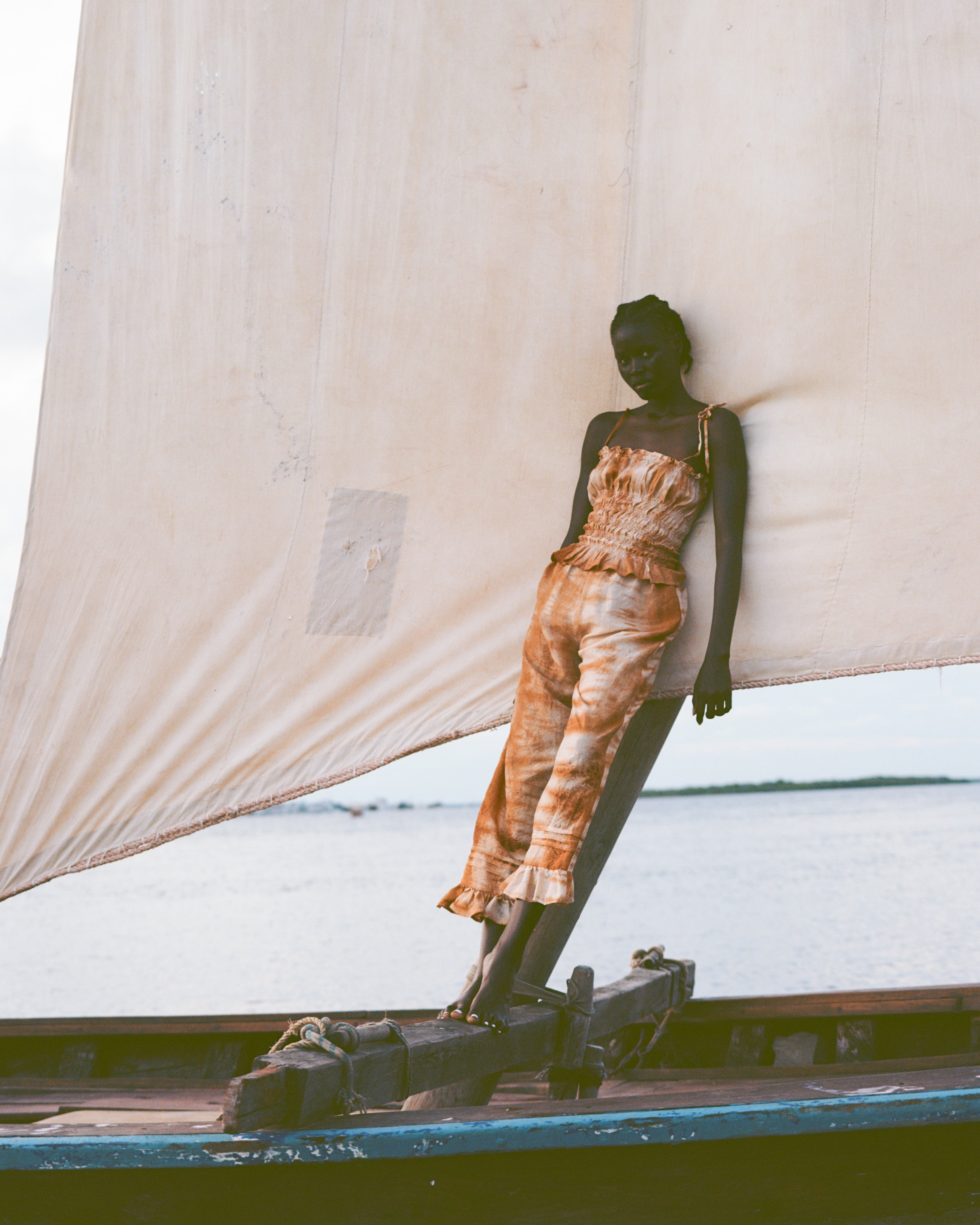Analog fashion portrait of model wearing HAMAJI on a traditional dhow boat in Lamu, Kenya, soft coastal light and sail backdrop