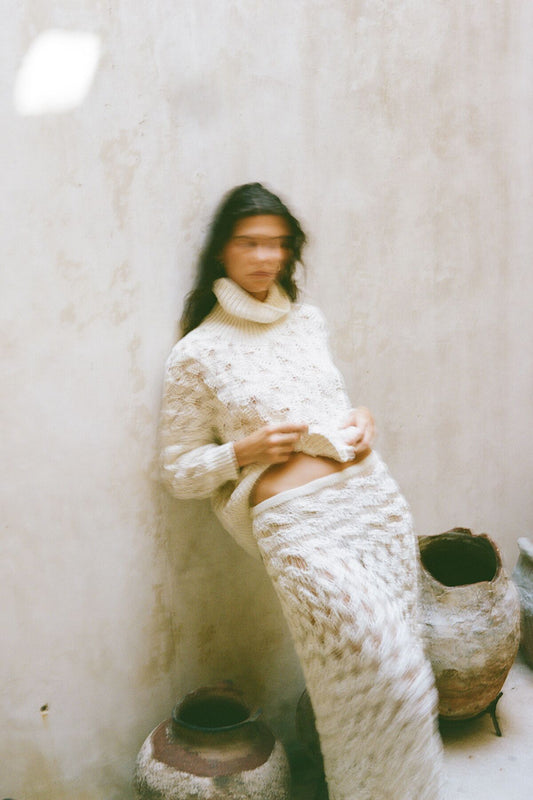 Analog fashion portrait of woman in soft knit cream outfit with motion blur, shot on 120mm film against textured neutral wall in natural light