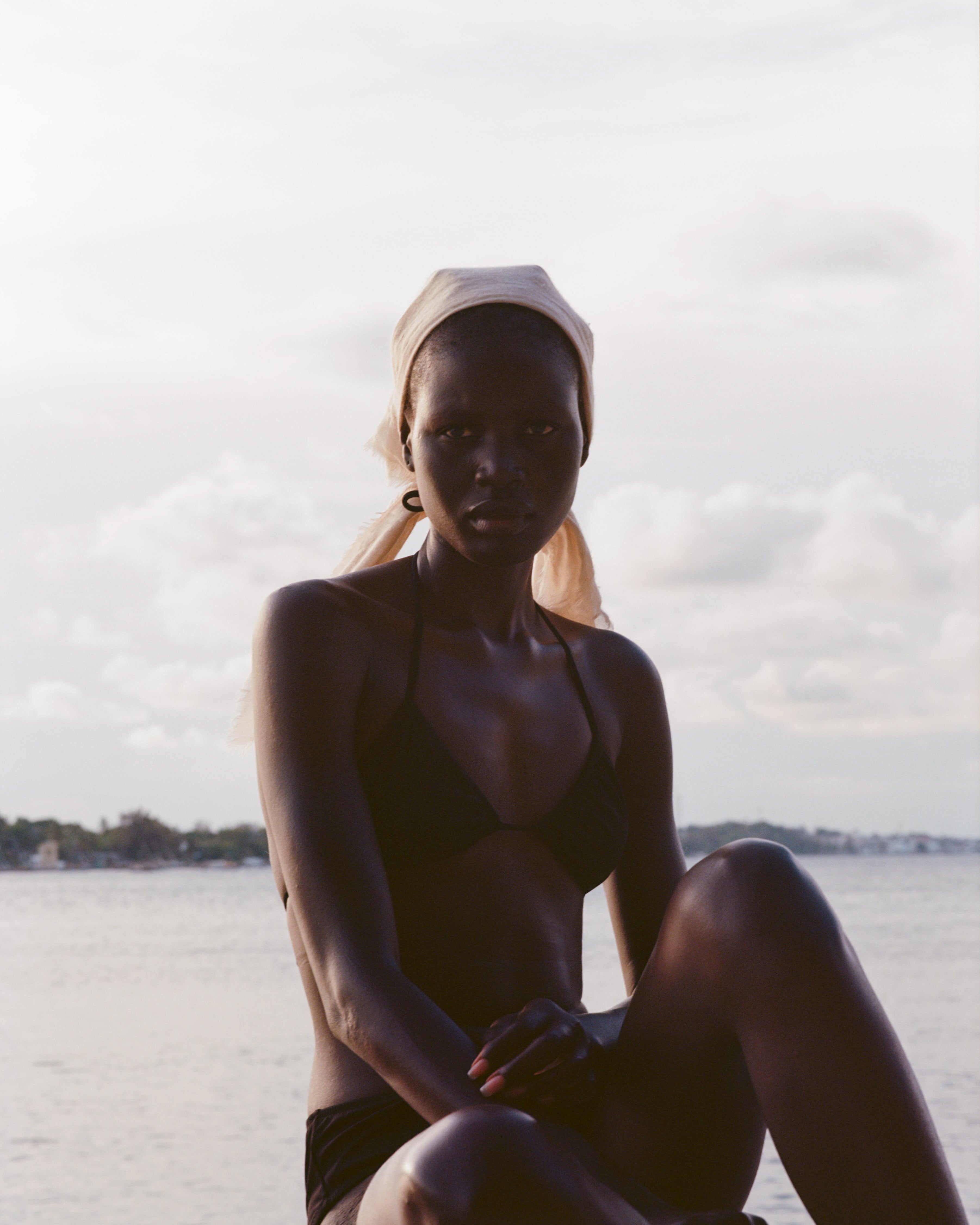 Analog fashion portrait of model in black bikini with headscarf by the ocean, shot on medium format film in soft natural light