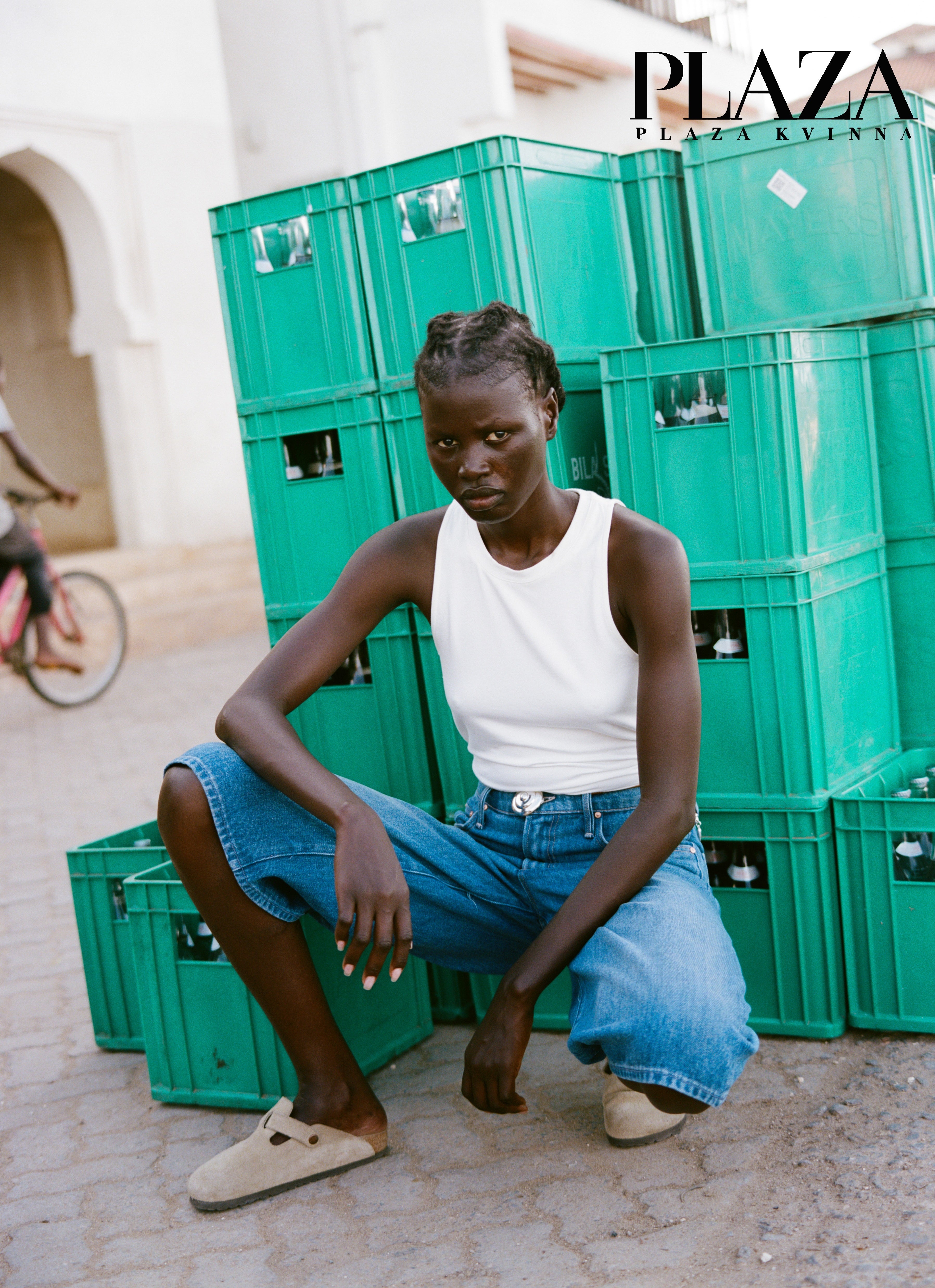Analog editorial fashion portrait of model seated against green crates, published in Plaza Magazine, shot on medium format film in Lamu, Kenya