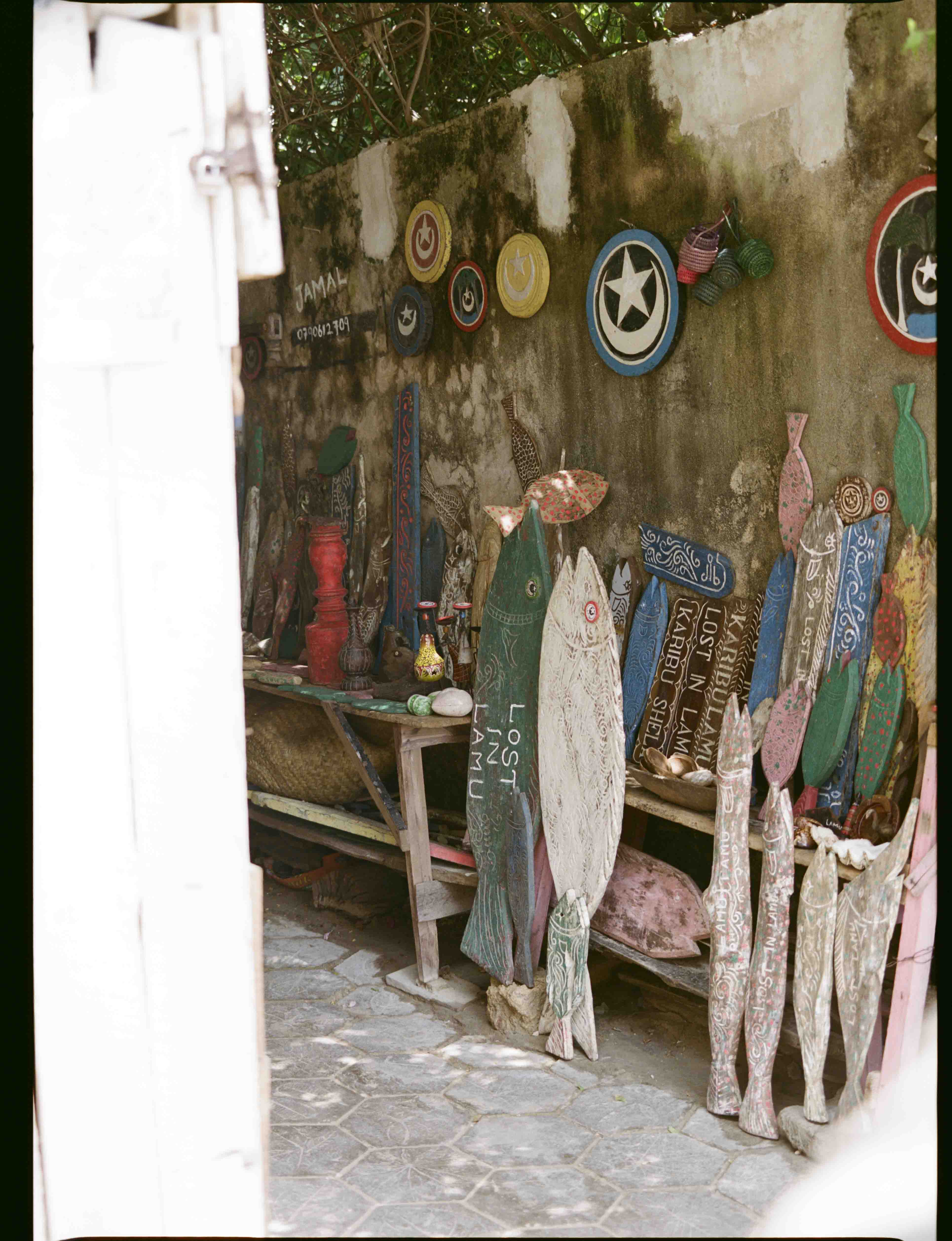 Analog image of vibrant handmade wooden fish and decorative objects arranged along a weathered wall in an outdoor setting, shot on 120mm film