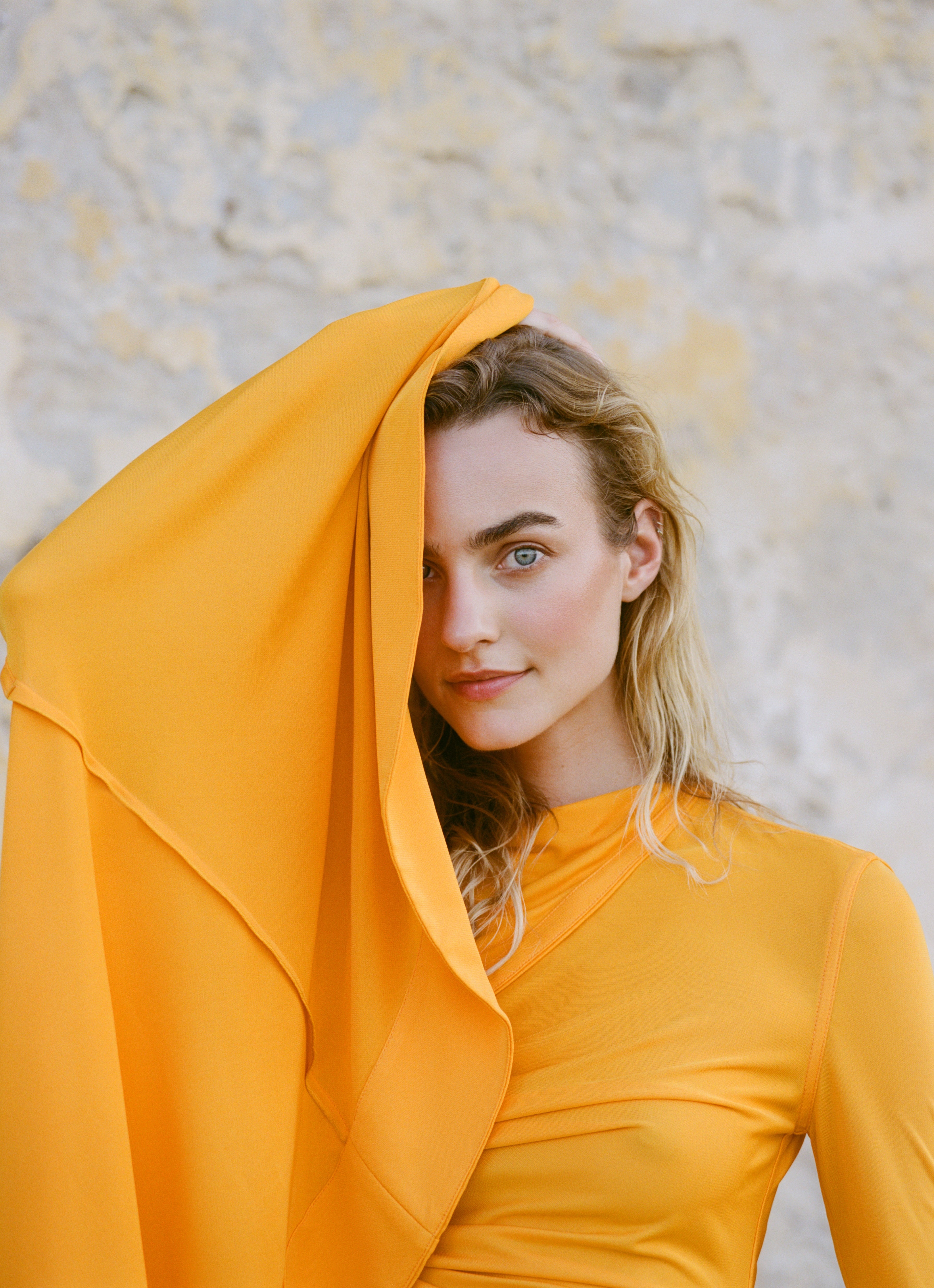 Analog fashion portrait of Maartje Verhoef in Bottega Veneta, wrapped in flowing orange fabric against a neutral textured backdrop, shot on medium format film