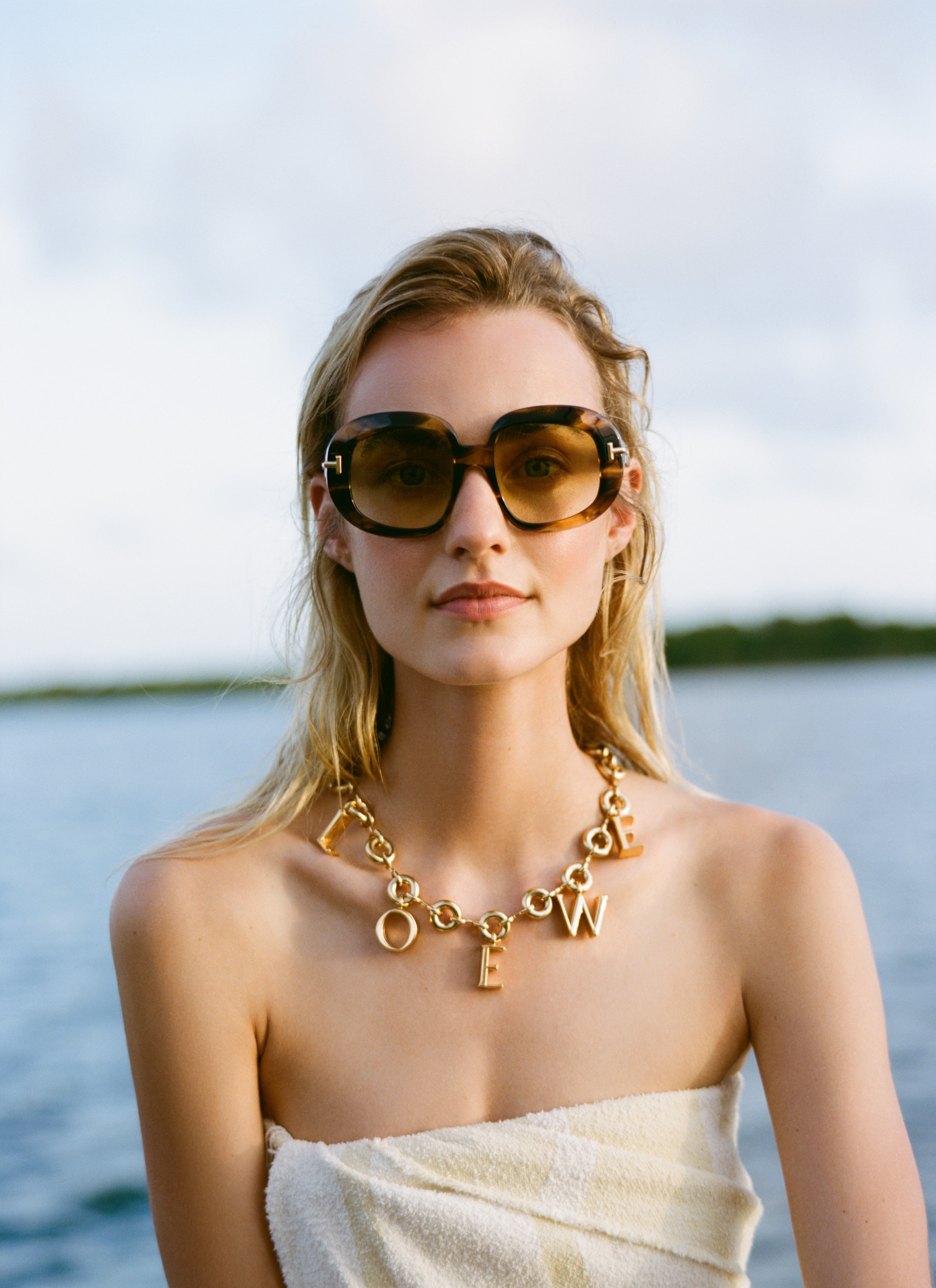 Analog fashion portrait of Maartje Verhoef wearing LOEWE sunglasses and gold necklace by the ocean, shot on medium format 120 film in natural light