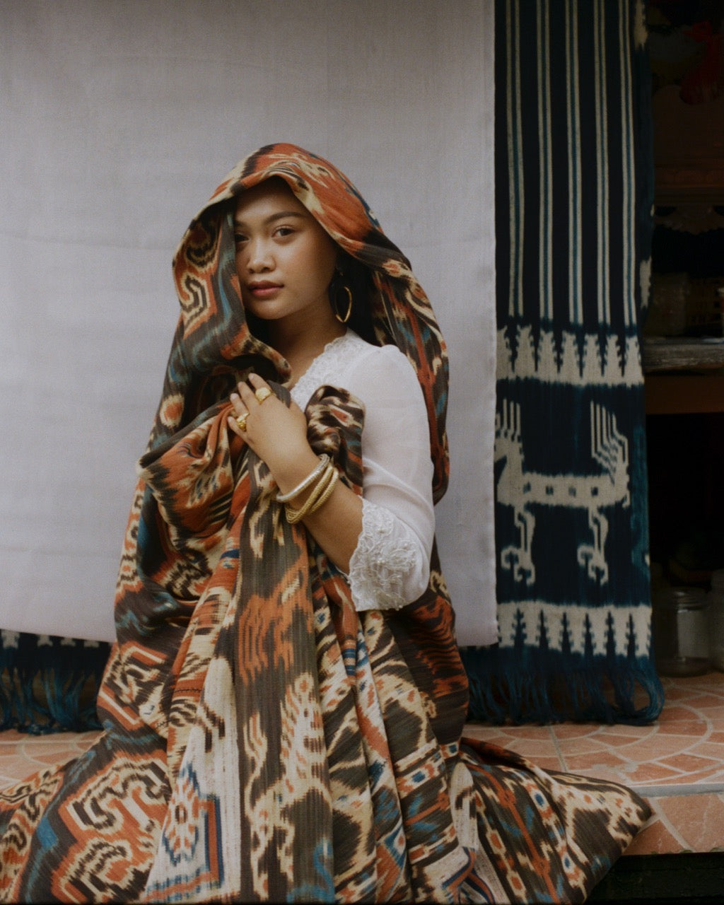 Analog portrait of woman wrapped in patterned textile in a traditional home in Bali, wearing local designer clothing, shot on medium format film
