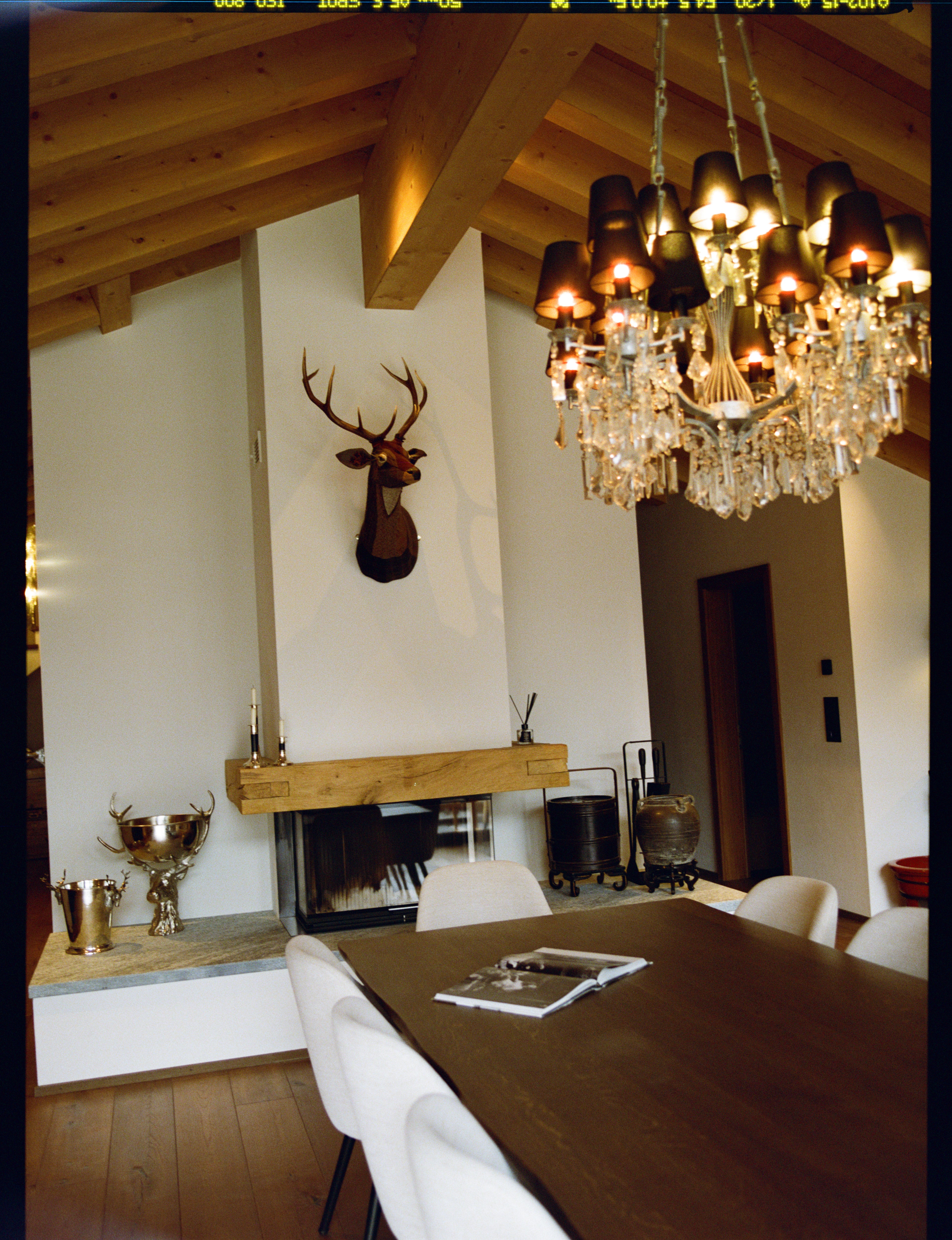 Analog interior photograph of alpine chalet dining room with wooden beams, chandelier, and fireplace, shot on medium format film