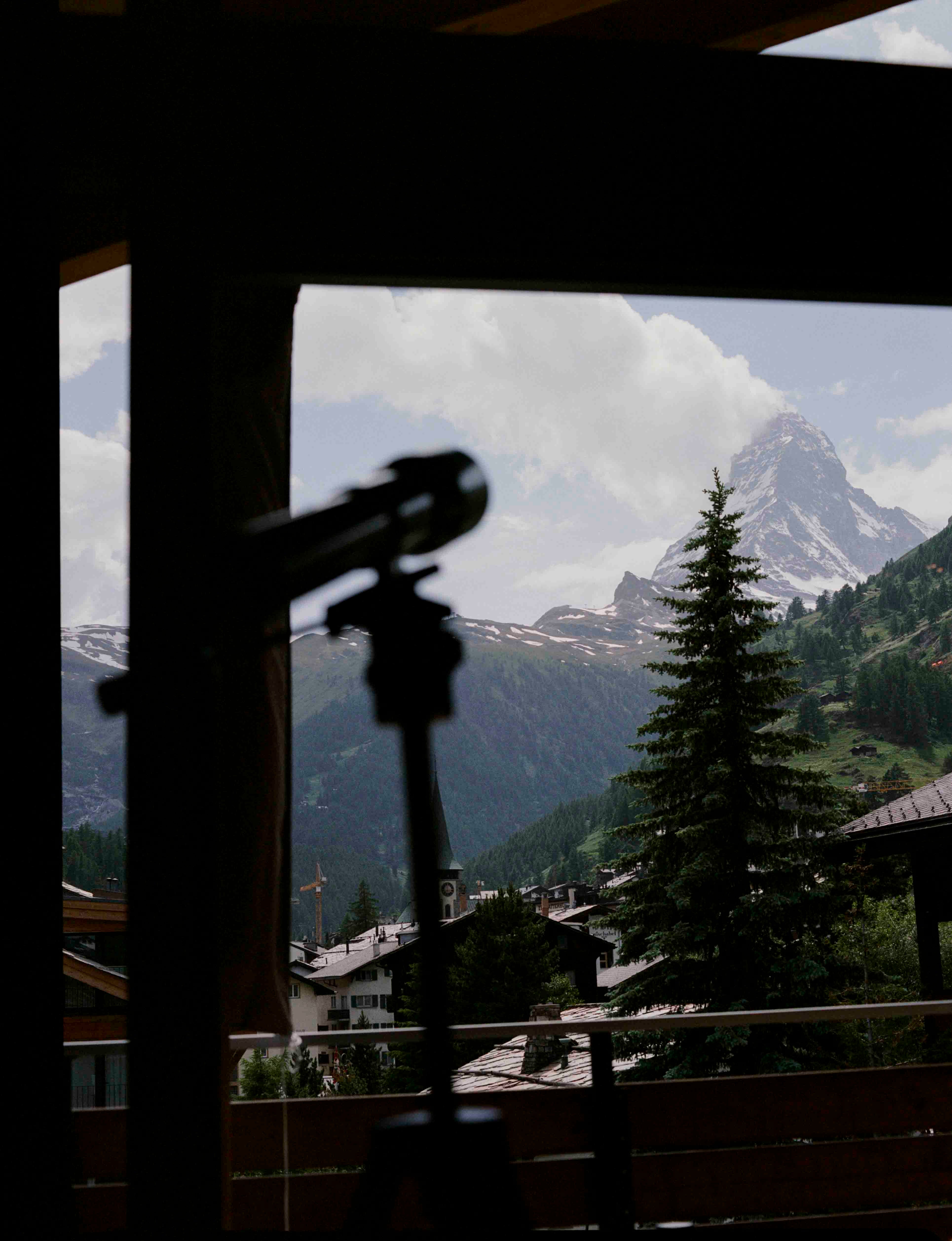 Analog view of the Matterhorn from a chalet in Zermatt, framed by interior with a telescope silhouette in the foreground, shot on medium format film