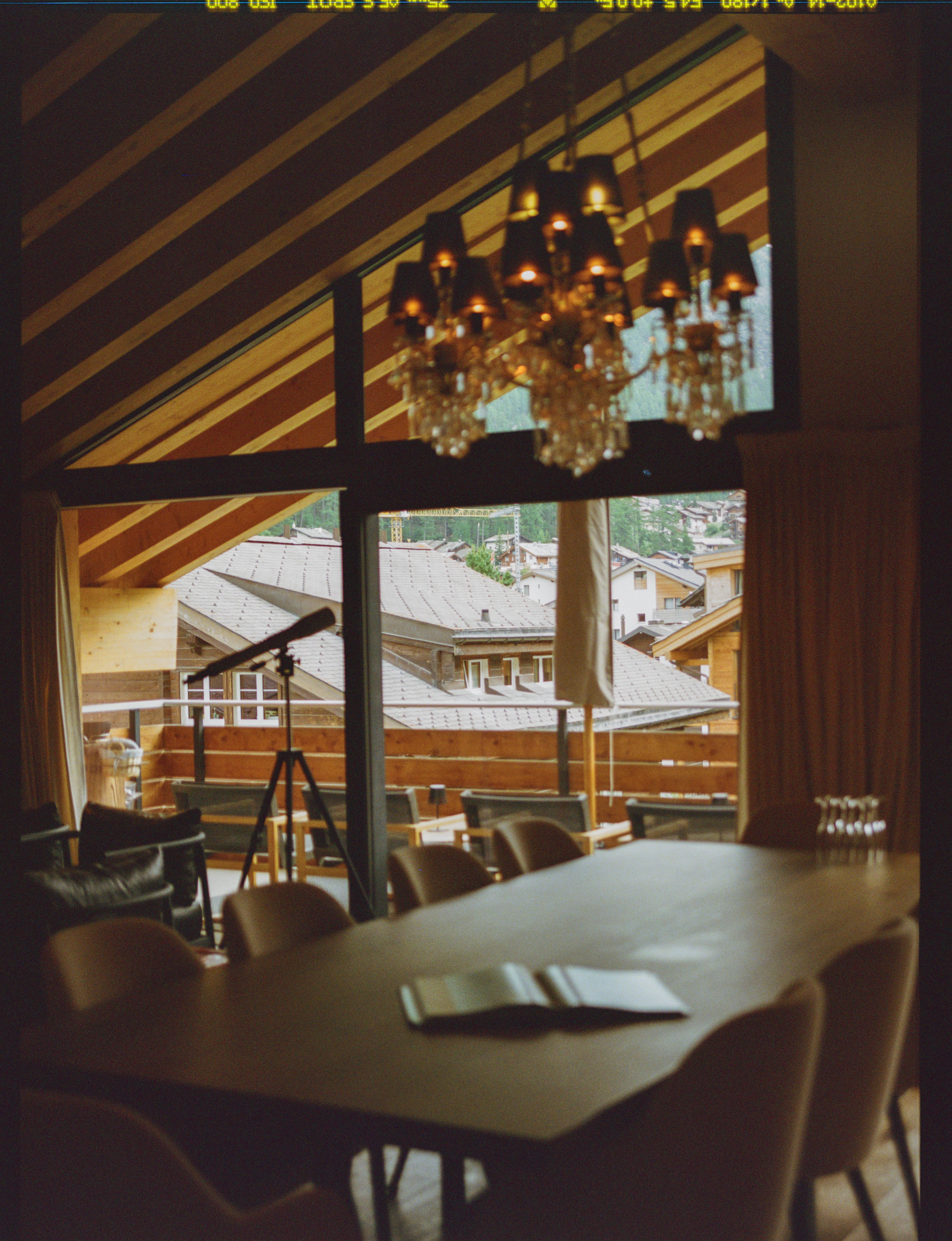 Analog interior photograph of dining space with chandelier and wooden architecture overlooking alpine village in Zermatt, shot on medium format film