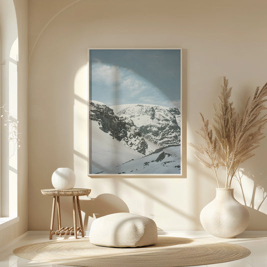 Minimalist interior with a framed snow-covered mountain landscape print in soft blue tones, styled above a wooden console with ceramic vases and natural light, fine art analog photography print shot on 35mm film