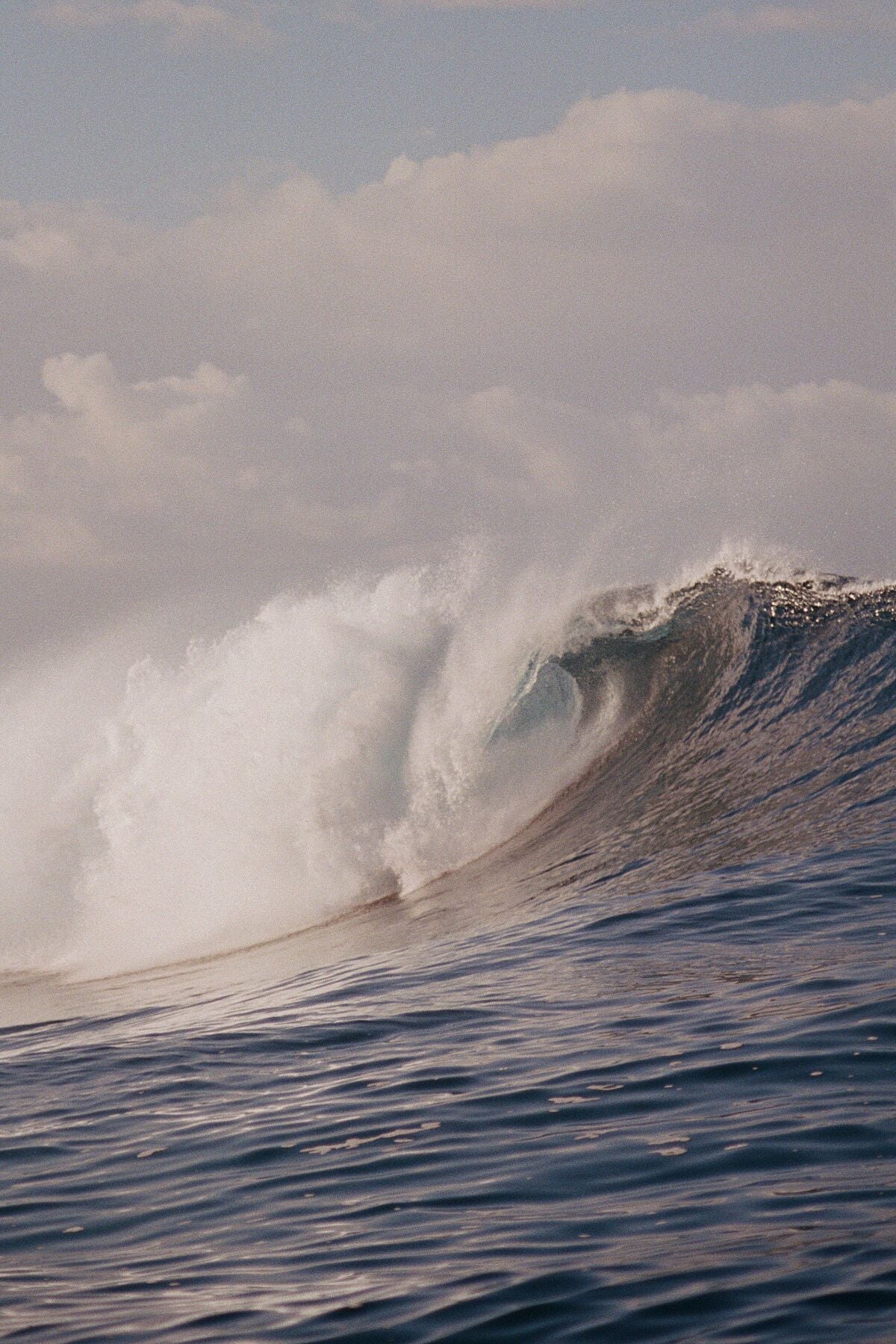 Analog ocean wave print of powerful breaking surf under soft light, shot on 35mm film with natural blue tones and cinematic texture