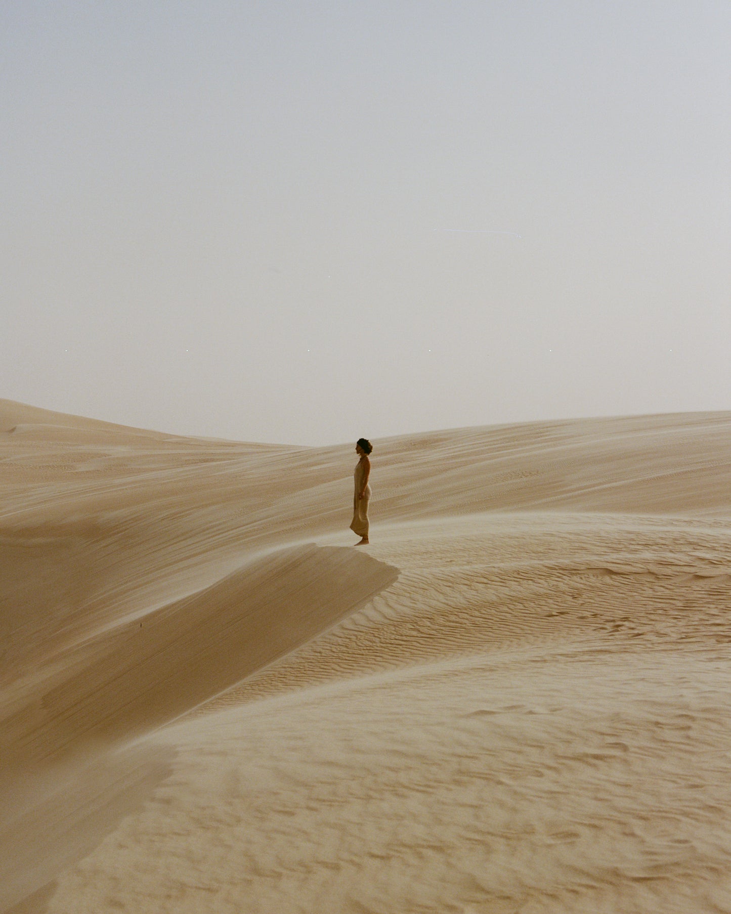 from the sahara series, analog print shot on medium format figure standing in the desert within a sand storm. 