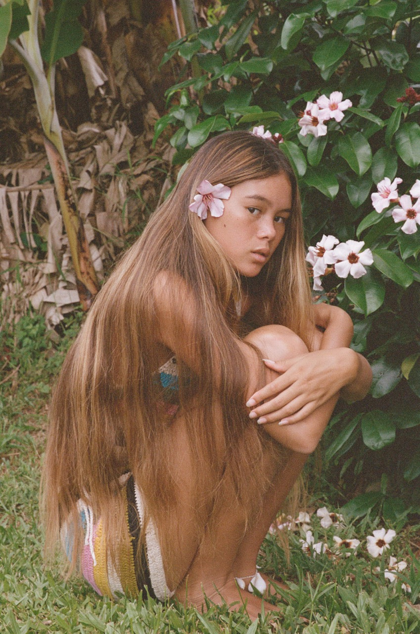 Analog portrait of model in tropical garden in Tahiti with flowers in her hair, shot on 35mm film in soft natural light